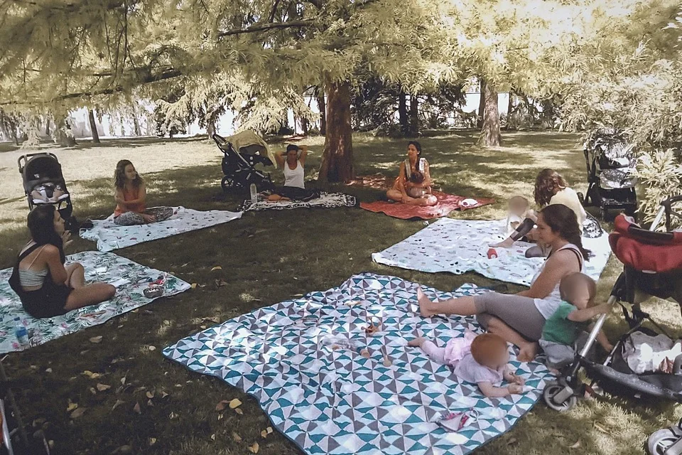Varias familias con sus bebés sobre mantas, en un parque a la sombra