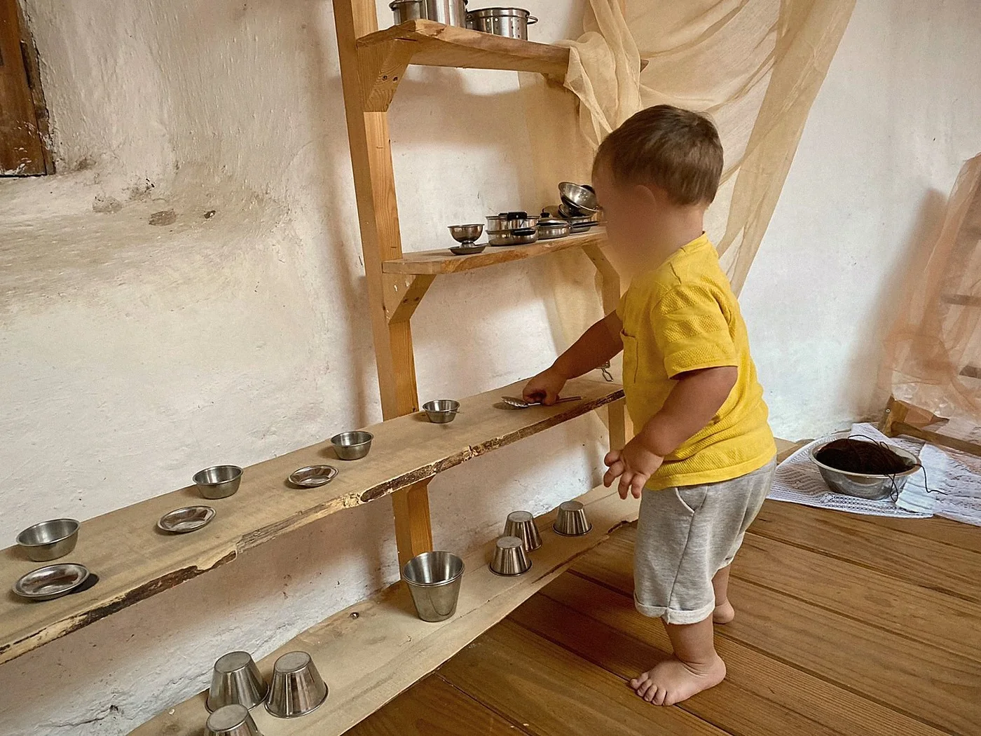 Una criatura de pie, descalza, eligiendo un cuenco de metal en una balda baja de madera dentro de un ambiente preparado