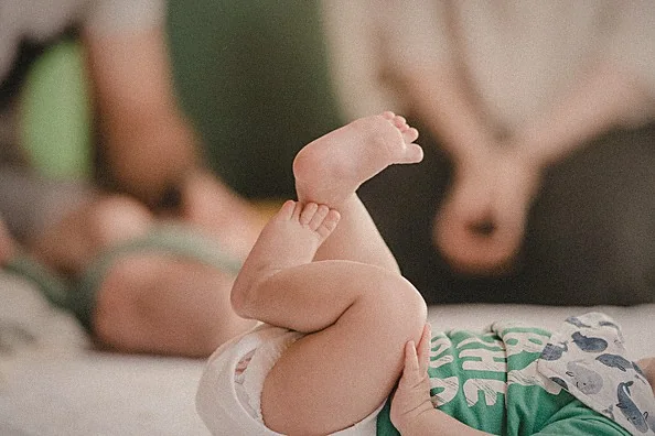 Un bebé tumbado boca arriba durante el cambio de pañal, con su madre y su padre desenfocados detrás